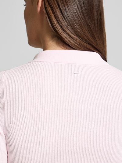 Vrouwenmodel draagt Slim Fit Poloshirt uit ribbreisel van BOSS in lichtroze met polokraag en 3-knoopssluiting, detailopname rug.