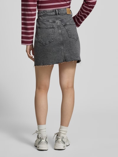 Frauenmodel trägt Regular Fit Jeansrock aus Baumwoll-Mix Modell 'TESSA' von Vero Moda in Denim-Optik, Mini-Länge, Label-Patch, 5-Pocket-Design, Materialverarbeitung Twill, Ganzkörperansicht Rückansicht.