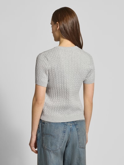 Frauenmodel trägt Kurzarmpullover mit Zopfmuster und Rundhalsausschnitt von Review, reine Baumwolle, Slim-Fit, Logo, Rippbündchen, Ganzkörperansicht Rückansicht.