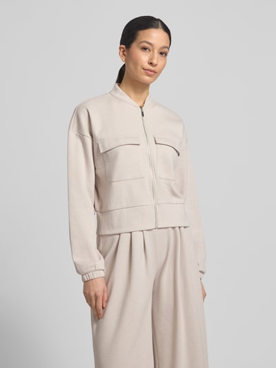Modelka kobieca ma na sobie Piqué Blouson Jacke mit Taschen od Christian Berg Woman w beżowym kolorze, mieszanka bawełny, prosta forma, stebnowane kieszenie na piersi, stójka, zamek, elastyczne mankiety, lekko teksturowany materiał, widok na górną część ciała z przodu.