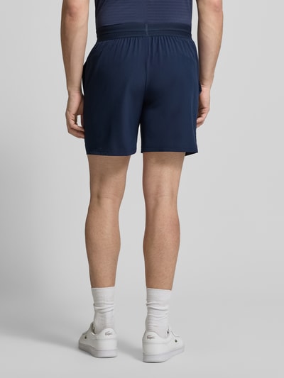 Männermodel trägt Loose Fit Sport-Shorts mit Mesh-Bund von Lacoste Sport in Dunkelblau, unifarben, elastischer Bund, Ganzkörperansicht Rückansicht.