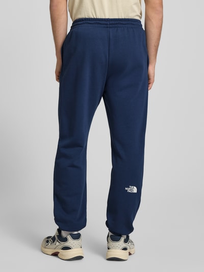 Männermodel trägt Sweatpants mit Logo-Print von The North Face in Dunkelblau, Baumwoll-Mix, elastischer Bund, Rückansicht Ganzkörperansicht.