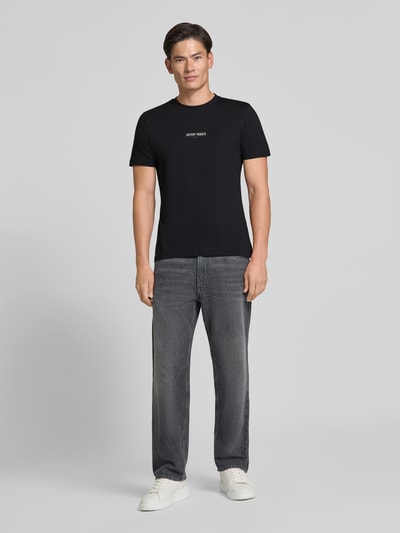 Männermodel trägt Regular Fit T-Shirt mit Label-Print von Antony Morato in Schwarz, kombiniert mit grauer Hose, Ganzkörperansicht von vorne.
