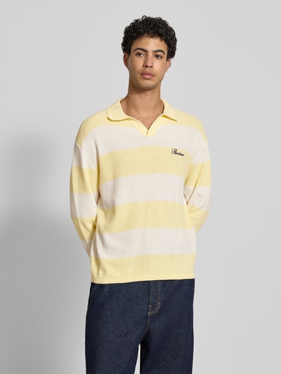 Männermodel trägt Regular Fit Strick-Poloshirt mit Block-Streifen von REVIEW aus reiner Baumwolle, gelb-weiß, Logo auf der Brust, Nahaufnahme Oberkörper.