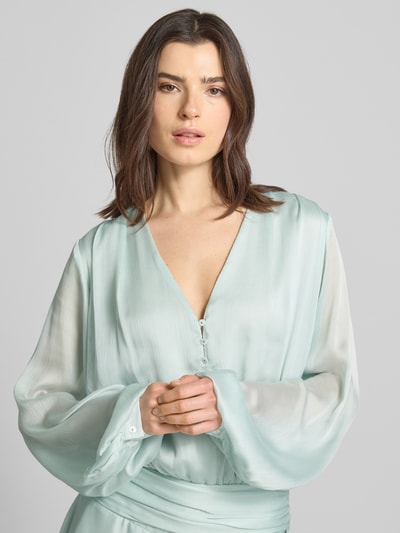 Frauenmodel trägt Minikleid mit kurzer Knopfleiste Modell 'MAGALI' von Guess in hellem Mint, V-Ausschnitt, Volantsaum, Nahaufnahme Oberkörper. Rückenlänge bei Größe S 88 cm, Brustweite 46 cm, Taillierter Schnitt, seitlicher Knopf- und Reißverschluss, Ärmellänge 72 cm.