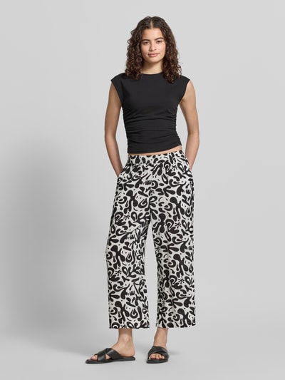 Frauenmodel trägt Weite HOSE aus reiner Viskose Modell 'BARRI' von Pieces mit Optik:Allover-Muster, grafischem Muster, 3/4-Länge, elastischem Bundabschluss, seitlichen Eingrifftaschen und glatter Textur, Schwarz-Weiß, Ganzkörperansicht von vorne.