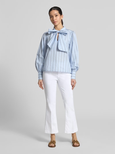 Kobiece modelka nosi białe bootcut jeansy w 5 kieszeni model 'Mary' od Brax, mieszanka bawełny i lyocellu z dodatkiem streczu, fason z rozszerzaną nogawką, detal z logo, szerokość w rozmiarze 36: 39 cm, długość wewnętrzna nogawki w rozmiarze 36: 67 cm, widok całej sylwetki z przodu.