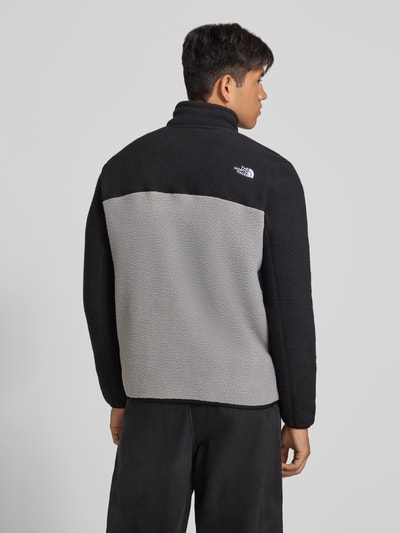 Männermodel trägt Fleecejacke mit Stehkragen Modell 'YUMIORI' von The North Face, Farbblock-Design in Schwarz und Grau, Ganzkörperansicht Rückansicht. Lockere Passform, elastische Abschlüsse, Kontext: Herren Fleecejacke, Seitentaschen mit Reißverschluss, Napoleontasche, Rückenlänge und Ärmellänge je 71 cm bei Größe M.