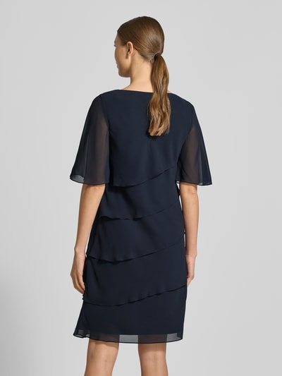 Frauenmodel trägt Relaxed Fit Kleid mit Ziersteinbesatz von Christian Berg Cocktail in Dunkelblau, halbarm, semitransparente Rüschen, blickdichter Unterrock, Ganzkörperansicht Rückansicht.