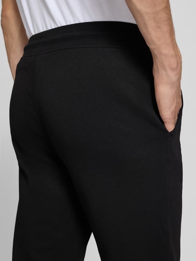 Mężczyznamodel nosi spodnie dresowe Sweatpants mit Label-Print Modell 'GORDON' od JACK & JONES, czarny, wpuszczane kieszenie, luźny krój, tunel w pasie, długość wewnętrzna nogawki w rozmiarze M: 77 cm, zbliżenie na tył KI-modifiziertes Bild