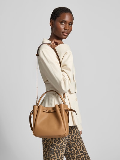 Frauenmodel trägt Bucket-Bag mit Logo-Detail von Tory Burch in Beige mit Strukturmuster, Magnetverschluss und Tunnelzug, Nahaufnahme Oberkörper. Breite 22 cm, Länge 22 cm, Tiefe 10 cm, abnehmbarer Schulterriemen, Hauptfach.