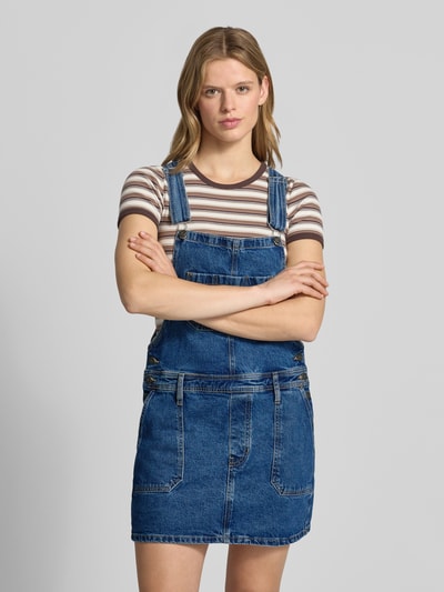 Frauenmodel trägt Jeanskleid mit Brusttasche und Label-Detail von Guess Jeans aus Baumwoll-Elasthan-Mix, Gerader-Schnitt, Minikleid, Eingrifftaschen, Verstellbarer-Träger, Ganzkörperansicht von vorne.