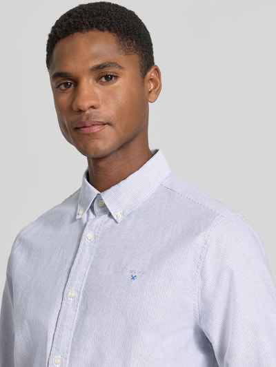 Mężczyzna nosi koszulę casualową model 'Striped Oxford' od Barbour, efekt: wzór na całej powierzchni, krój tailored fit, kołnierzyk typu button down, listwa guzikowa na całej długości, fakturowany wzór, wyhaftowane logo, długi rękaw, sportowe mankiety z regulowanymi guzikami, wykończenie materiału: oxford, materiał: czysta bawełna, kolor jasnoniebieski, drobne paski, Nahaufnahme oberkörper.