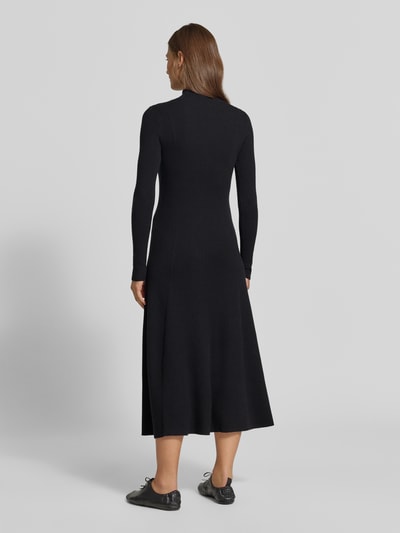 Frauenmodel trägt Strickkleid aus Viskose-Mix in Midilänge von MYON in Schwarz, eng anliegend, Rockteil A-Linie, Stehkragen, Ripp-Optik, langärmelig, Rückenlänge 125 cm, Brustweite 45 cm, Ärmellänge 65 cm, Ganzkörperansicht Rückansicht.