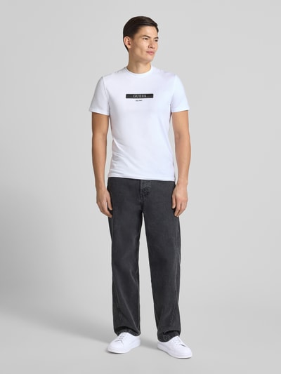 Männermodel draagt T-Shirt mit Label-Detail van Guess in wit, regular fit, geribde ronde hals, katoenen mix, Ganzkörperansicht van voren.