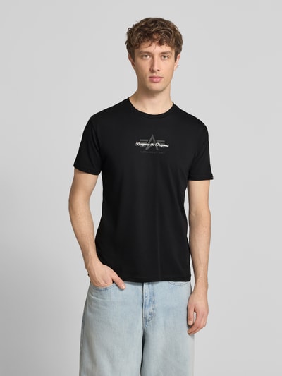 Mężczyzna nosi T-Shirt mit Label-Detail Modell 'Foam' od Alpha Industries, czarny kolor, czysta bawełna, krój regular fit, widok z przodu, ujęcie całej sylwetki.