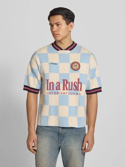 Männermodel trägt Strickshirt mit Label-Stitching Modell 'Victory' von PROHIBITED in Beige und Hellblau, reine Baumwolle, Relaxed Fit, Ganzkörperansicht von vorne.