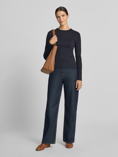Frauenmodel trägt Slim Fit Longsleeve aus reiner Baumwolle Modell 'NURIT' von DRYKORN, dunkelblau mit feinen Streifen, kombiniert mit weiter Jeans und brauner Umhängetasche, Obermaterial weich strukturiert, Rundhalsausschnitt, Rückenlänge bei Größe S 57 cm, Ganzkörperansicht von vorne.