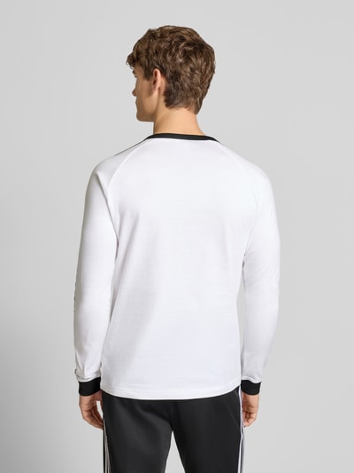 Männermodel trägt Longsleeve mit Label-Stitching von adidas Originals in Weiß mit schwarzen Details, Baumwolle, Regular Fit, Ganzkörperansicht Rückansicht.