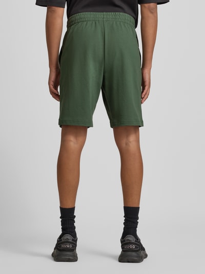 Männermodel trägt Shorts mit elastischem Bund und Logo von EA7 Emporio Armani in Dunkelgrün, Reine Baumwolle, Regular-Fit, Ganzkörperansicht Rückansicht.