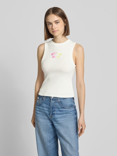 Frauenmodel trägt Slim Fit Top aus Baumwoll-Mix von Tommy Jeans in Weiß mit Label Print, breite Träger, Rippenstruktur, Ganzkörperansicht von vorne.