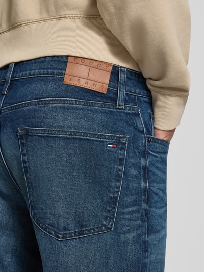 Männermodel trägt Tapered Fit Jeans aus Baumwoll-Mix von Tommy Jeans in Dunkelblau mit braunem Lederlabel, Nahaufnahme Rückansicht, Herren Tapered Fit Jeans von Tommy Jeans.