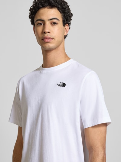 Męski model nosi Regular Fit T-Shirt mit Logo-Stitching von The North Face z bawełnianej mieszanki, biały kolor, okrągły dekolt, szerokość w rozmiarze M: 70 cm, zbliżenie na górną część ciała