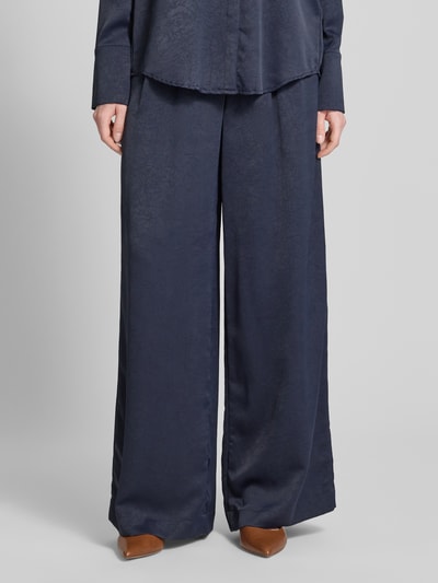 Kobiece model nosi Wide Fit Stoffhose mit Strukturmuster od Christian Berg Cocktail, fakturowany wzór, kwiatowy wzór, krój wide fit, zakładki w pasie, zapięcie na haftkę i zamek błyskawiczny, szerokość w rozmiarze 36: 40 cm, długość wewnętrzna nogawki w rozmiarze 36: 80 cm, ciemnoniebieski kolor, gładka tekstura, widok całej sylwetki z przodu.