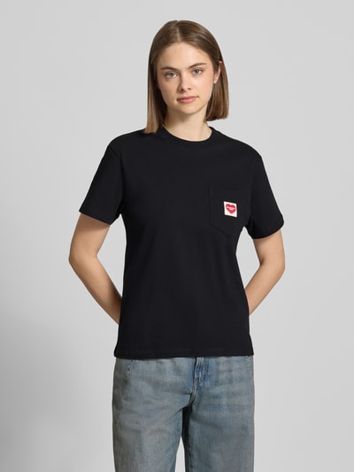 Kobiece modelka nosi damski t-shirt z bawełny, prosty krój, okrągły dekolt, brustasza z naszywką z logo, Carhartt Work In Progress, długość tyłu w rozmiarze S: 58 cm, widok całej sylwetki z przodu.