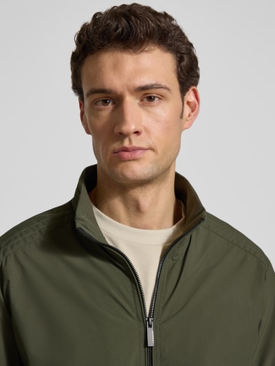 Männermodel trägt Regular Fit Jacke mit Stehkragen von Lerros in Olivgrün, glatte Textur, Logo-Detail, Nahaufnahme Oberkörper.