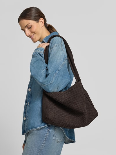 Frauenmodel trägt eine schwarze Handtasche mit Webmuster und Schulterriemen von COMMA, kombinierbar zu Jeans, Nahaufnahme Oberkörper. Damen Handtasche mit Magnetverschluss, Innenfach mit Reißverschluss, Maße 48x30x10 cm, Schulterriemen 78 cm.