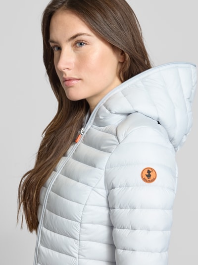 Frauenmodel trägt Slim Fit Steppjacke im Zweiwegereißverschluss Modell 'Daisy' von SAVE THE DUCK in Stepp-Optik mit Kapuze, Nahaufnahme Oberkörper.