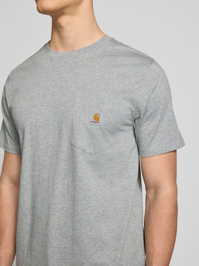 Männermodel trägt Regular Fit T-Shirt mit Logo-Patch von Carhartt Work In Progress in Grau aus Reine Baumwolle mit Brusttasche, Nahaufnahme Oberkörper.