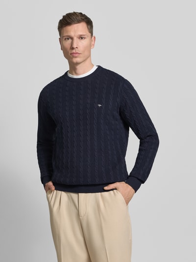 Männermodel trägt Strickpullover mit Zopfmuster und Label-Stitching von Fynch-Hatton, Reine Baumwolle, Slim-Fit, Rundhalsausschnitt, Dunkelblau, Ganzkörperansicht von vorne.