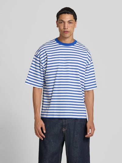 Männermodel trägt Oversized T-Shirt mit Label-Stitching von REVIEW, blaue und weiße Streifen, Reine Baumwolle, Allover-Look, Rundhalsausschnitt, Rückenlänge bei Größe M 67 cm, Ganzkörperansicht von vorne.