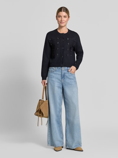 Frauenmodel trägt Cardigan aus Viskose-Mix mit Zierknöpfen Modell 'GENIO' von MANGO in Schwarz, kombiniert mit blauer Jeans, Ganzkörperansicht von vorne.