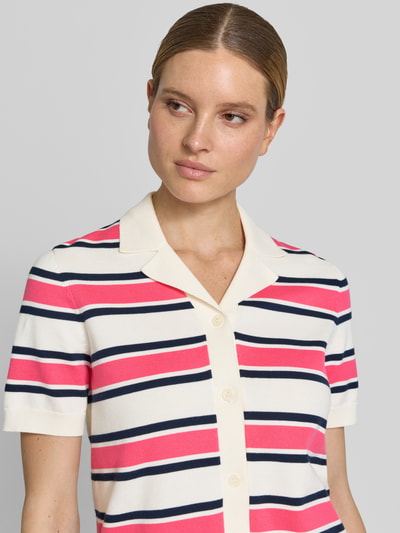 Frauenmodel trägt Regular Fit Poloshirt aus reiner Bio-Baumwolle Modell 'AMOUR' von Selected Femme, gestreift in Pink, Navy und Creme, kurzer Arm, Polokragen, Strickstruktur, Label Print, Nahaufnahme Oberkörper.
