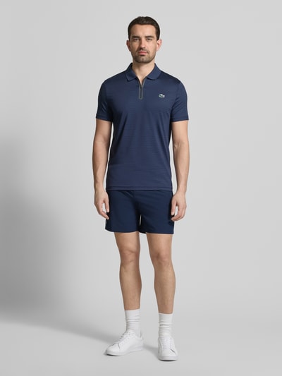 Männermodel trägt Loose Fit Sport-Shorts mit Mesh-Bund von Lacoste Sport, unifarben, Logo-Stitching, Ganzkörperansicht von vorne.