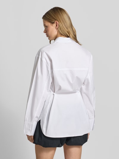 Frauenmodel trägt Oversized Hemdbluse mit Brusttasche Modell 'Demi' von Topshop aus reiner Baumwolle, langärmelig, weiße Farbe, Umlegekragen, durchgehende Knopfleiste, Rückenlänge 77 cm, lockerer Schnitt, Ganzkörperansicht Rückansicht.