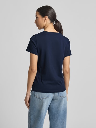 Modelka kobieca ma na sobie Regular Fit T-Shirt aus Bio-Baumwoll-Mix od Tom Tailor, gładka optyka, krótki rękaw, detalowy napis, jasnoniebieskie jeansy, widok całej sylwetki z tyłu.