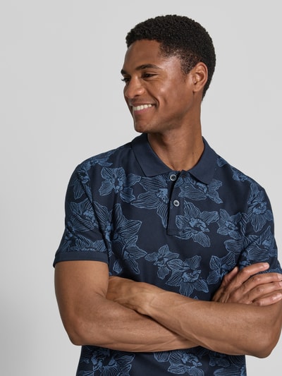 Männermodel trägt Slim Fit Poloshirt mit floralem Allover-Print von Lerros aus Reiner Baumwolle, dunkelblau, Nahaufnahme Oberkörper.