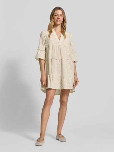 Vrouwenmodel draagt Vero Moda Ausgestelltes Blusenkleid aus reiner Baumwolle Modell 'DICTHE' met all-over motief, henley-halslijn, trompetmouwen en mini lengte, rechte pasvorm, lichte katoen structuur, frontale volledige lichaamsweergave.