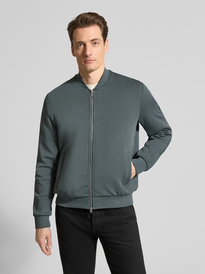 Mannenmodel draagt Regular Fit Bomberjacke aus Baumwoll-Mix van Marc O'Polo in effen katoenmix met collegekraag, rits, label patch, geribde boorden, lange mouw, steekzakken, frontale volledige lichaamsaanzicht.