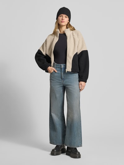Frauenmodel trägt Fleecejacke mit Zweiwege-Reißverschluss Modell 'CUDDLE' von Noisy May, Relaxed-Fit, Stehkragen, beige-schwarz, Damen, Nahaufnahme Ganzkörperansicht von vorne, Rückenlänge 55 cm, Schulterbreite 50 cm, Brustweite 61 cm, Ärmellänge 60 cm, grobe Struktur.