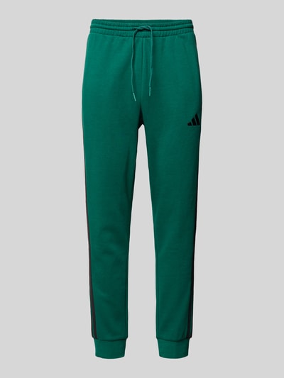 Produktfoto, grüne Sweatpants mit elastischem Bund von adidas Sportswear aus Baumwoll-Mix mit Viskose-Anteil, lockerem Schnitt, Tunnelzug, Label-Stitching und einer Innenbeinlänge von 76 cm bei Größe M.
