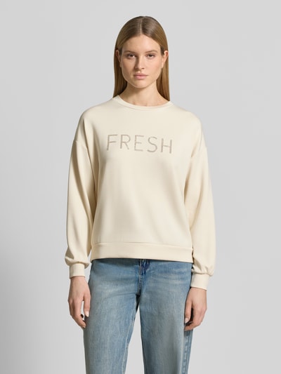 Kobiece modelka nosi Regular Fit Sweatshirt mit Ziersteinbesatz Modell 'Banu' od Soyaconcept, jasny beż z napisem i gumkami, elastyczny materiał z modalem, widok całej sylwetki z przodu.