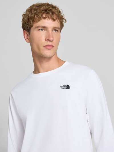 Męski model nosi bluzkę z długim rękawem z mieszanki bawełny Model 'EVOLUTION' od The North Face, wyhaftowane logo, luźny krój, białe kolory, długość tyłu w rozmiarze M: 70 cm, wygodne elastyczne wykończenia, wyraźna tekstura, półzbliżenie na górną część ciała.
