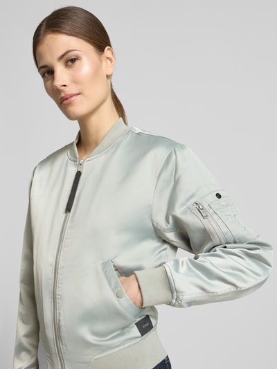 Modelka kobieca ma na sobie Regular Fit Bomberjacke mit Stehkragen Modell 'Beth' od khujo w jasnoszarym kolorze, z elastycznym materiałem, kieszeniami i zamkiem błyskawicznym, kontekst: damska bomberka, długość tyłu w rozmiarze S: 54 cm, szerokość ramion w rozmiarze S: 46 cm, szerokość klatki piersiowej w rozmiarze S: 47 cm, długość rękawa w rozmiarze S: 58 cm, zbliżenie na górną część ciała z przodu.