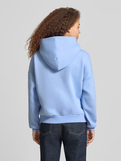 Frauenmodel trägt Hoodie mit Logo und Känguru-Tasche von Review in Hellblau, Baumwoll-Mix, Relaxed Fit, Ganzkörperansicht Rückansicht.