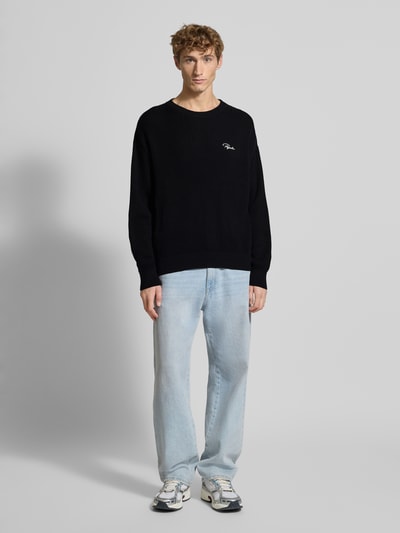 Männermodel trägt schwarzen Strickpullover mit gerippten Abschlüssen von Pegador, reine Baumwolle, Oversized, Ganzkörperansicht von vorne.